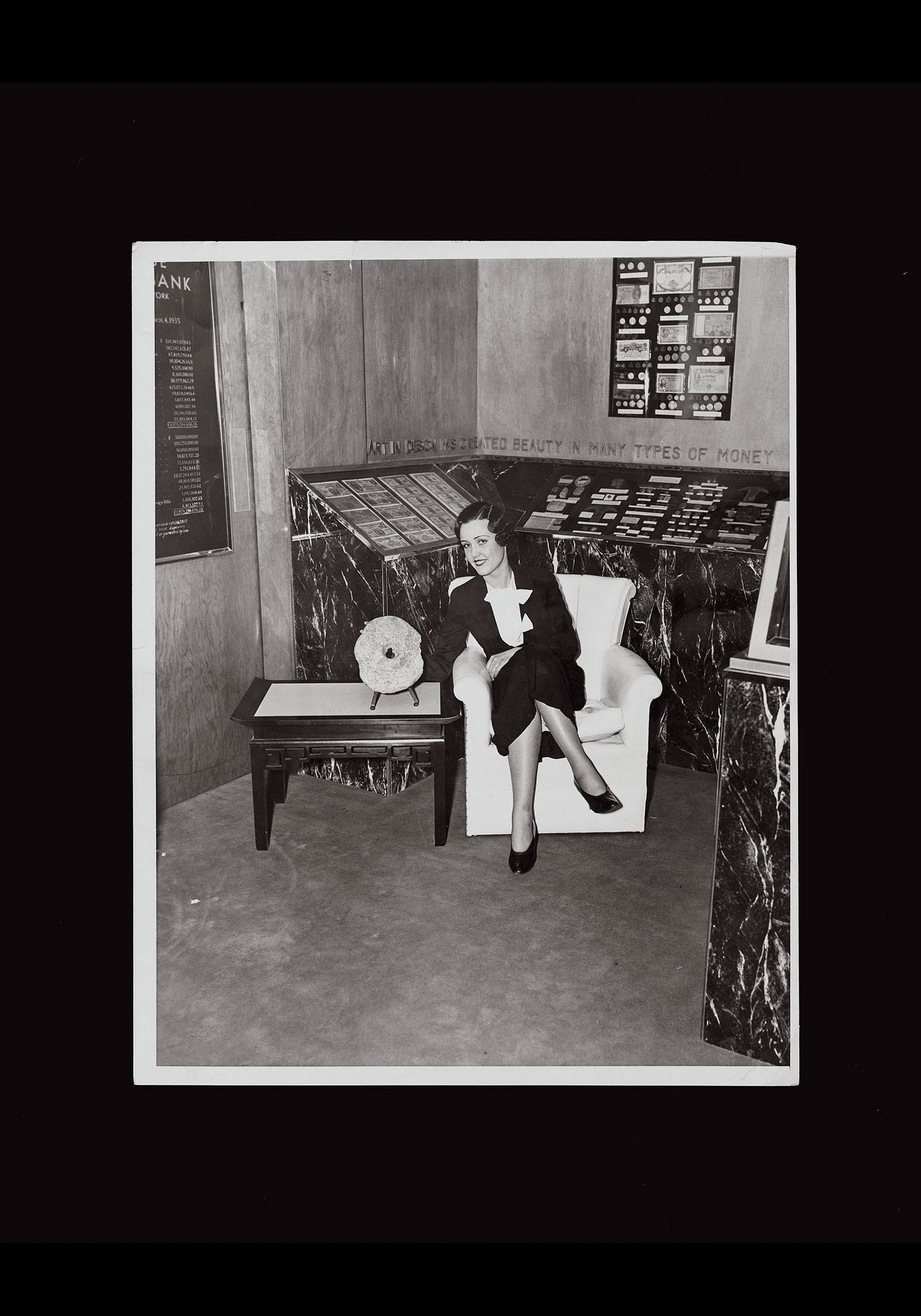 Miss Verna Long poses with a 12 pound Rai stone from the island of Yap at the Chase National Bank exhibit, 1935. Cut-line reads “Miss Verna Long, who is a typical consumer at the Industrial Arts Exposition, learns that a 12 pound stone coin from the island of Yap will buy 500 coconuts but is a bit awkward for pockets and purses, while she inspects specimens of curious and historic monies at the Chase National Bank exhibit in the Exposition.” Photographer unknown. Collection of Nicholas Mangan.